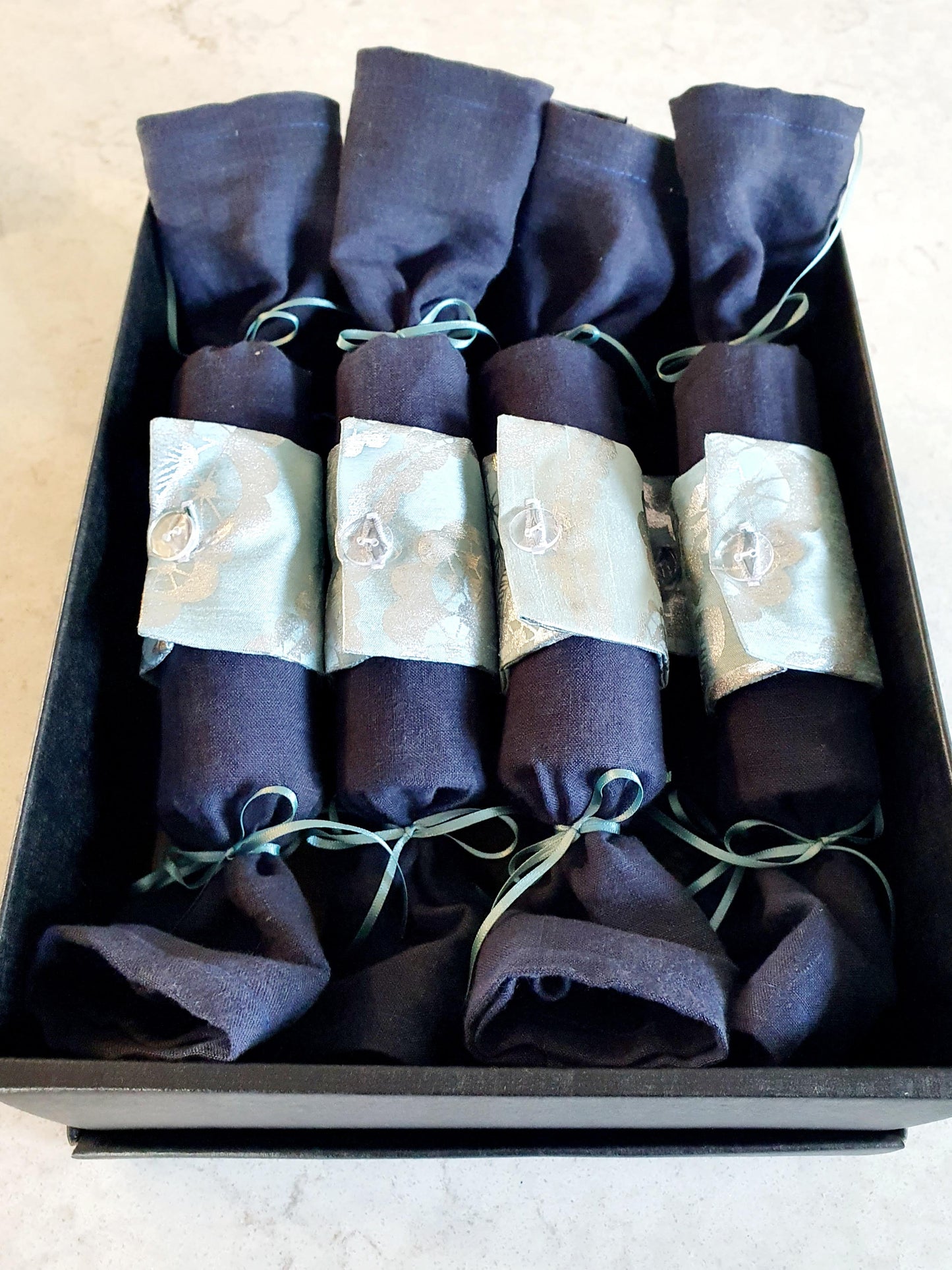 Fabric Christmas Cracker with Navy coloured base and pale turquoise with silver pattern cuff with clear buttons and turquoise ribbon, in black storage box