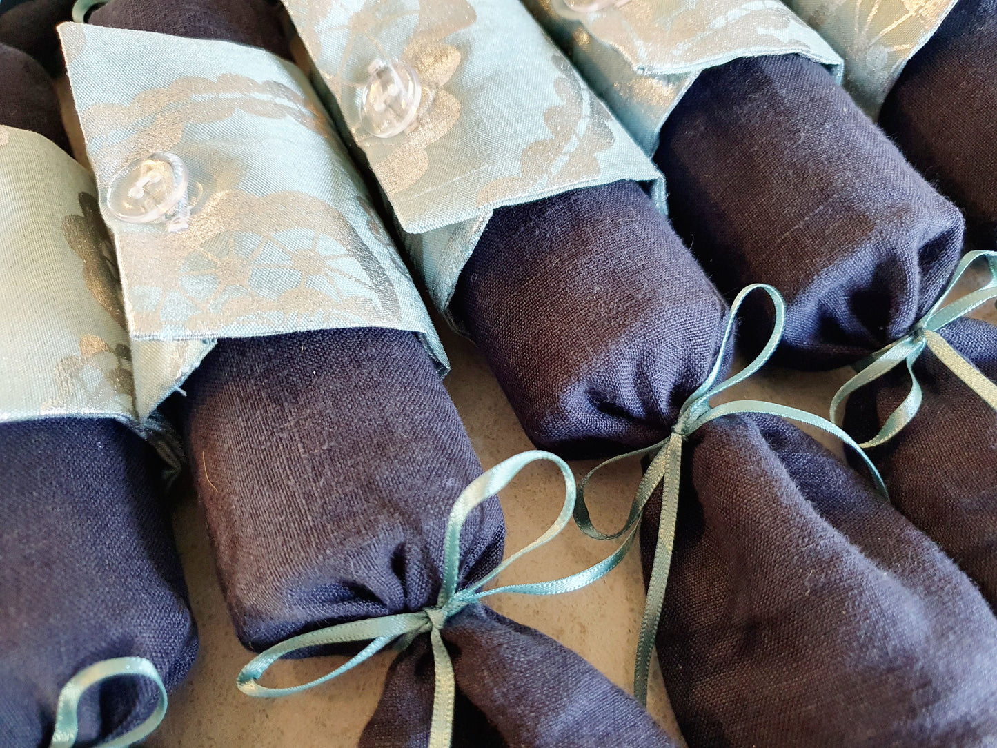 Close up of fabric Christmas Cracker with Navy coloured base and pale turquoise with silver pattern cuff with clear buttons and turquoise ribbon.